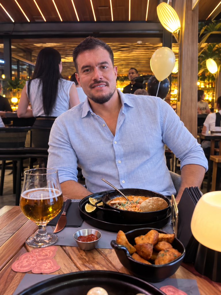 Rolando dining at Casa Eterna near Medellín, wearing a light blue linen shirt, with food and a beer on the table.